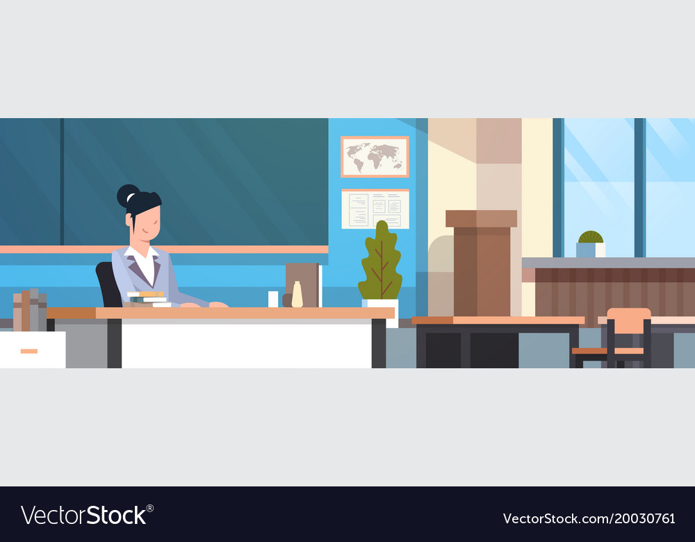 Female Teacher Sitting At Desk Over Chalk Board In